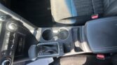Close view of a car's front interior showing the gear shifter, cup holders, and climate controls on the center console, with a red seat belt buckle on the passenger side.