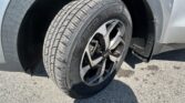 Close-up of a car tire and rim under the wheel well on a paved surface, showing tread pattern and black alloy wheel.