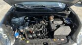 Car engine bay with the hood raised, showing the engine, hoses, battery, and coolant reservoir visible in the front compartment.