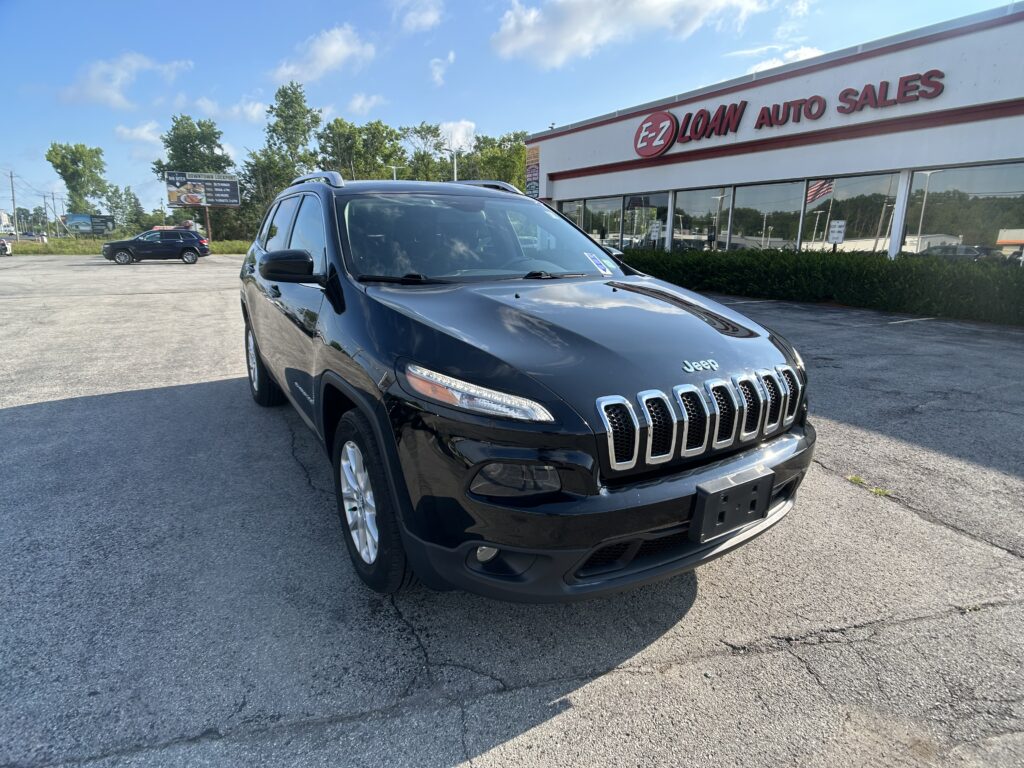Black Jeep SUV parked in front of EZ Loan Auto Sales on a sunny day, with the dealership sign visible in the background.
