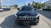 Front view of a black Jeep SUV (Grand Cherokee) parked in a dealership lot on a sunny day with other cars and a building in the background.
