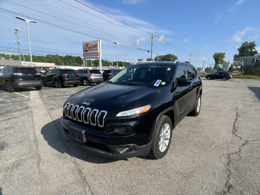 Black Jeep SUV in foreground at a daytime car dealership lot with other vehicles and an EZ Loan Auto Sales sign nearby