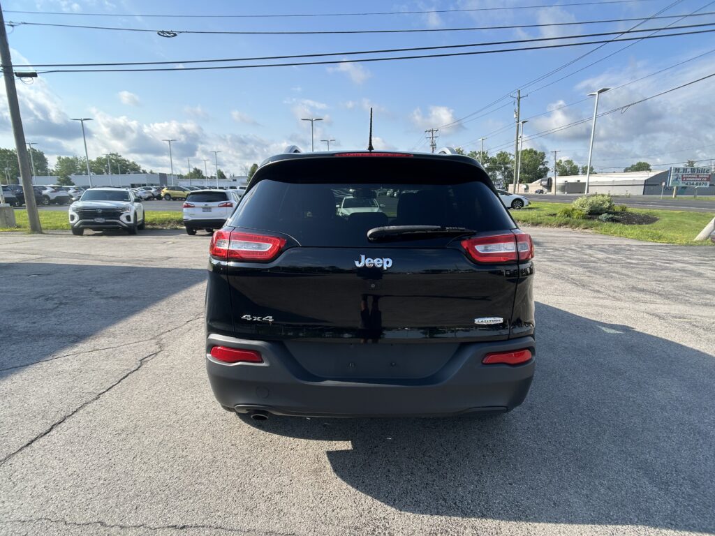 Rear view of a black Jeep Latitude 4x4 in a parking lot with other cars and a blue sky above.