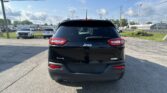 Rear view of a black Jeep Latitude 4x4 in a parking lot with other cars and a blue sky above.