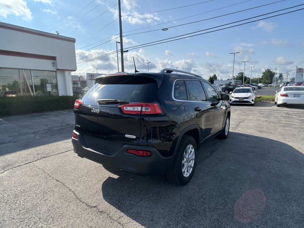 Black Jeep SUV in the foreground of a car dealership lot on a sunny day, with a Toyota dealership building and many cars in the background.
