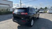 Black Jeep SUV in the foreground of a car dealership lot on a sunny day, with a Toyota dealership building and many cars in the background.