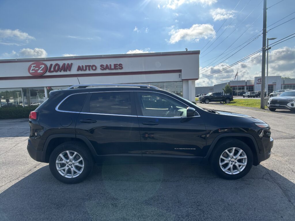Black Jeep Cherokee parked in front of E-Z Loan Auto Sales on a sunny day.