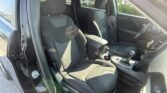 View of a car's front seating area from the open driver's side door; two dark fabric seats, center console, and gear shifter visible with sunlight glare inside the cabin.