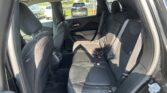 Rear passenger area of a black SUV with dark fabric seats and visible seat belts, looking toward the back seats from the open rear door; outside cars and a street are visible through the windows.