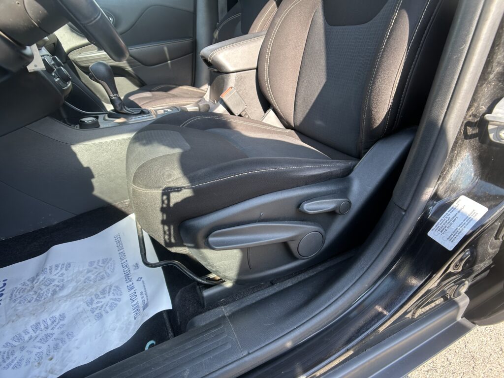 Interior of a car showing the front passenger seat and center console with gear shifter, handbrake, and cup holder; a paper floor mat lies on the floor near the door.