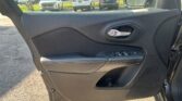 Car door interior: black padded panel with chrome door handle and window controls; outside view shows a parking lot with cars across the lot.
