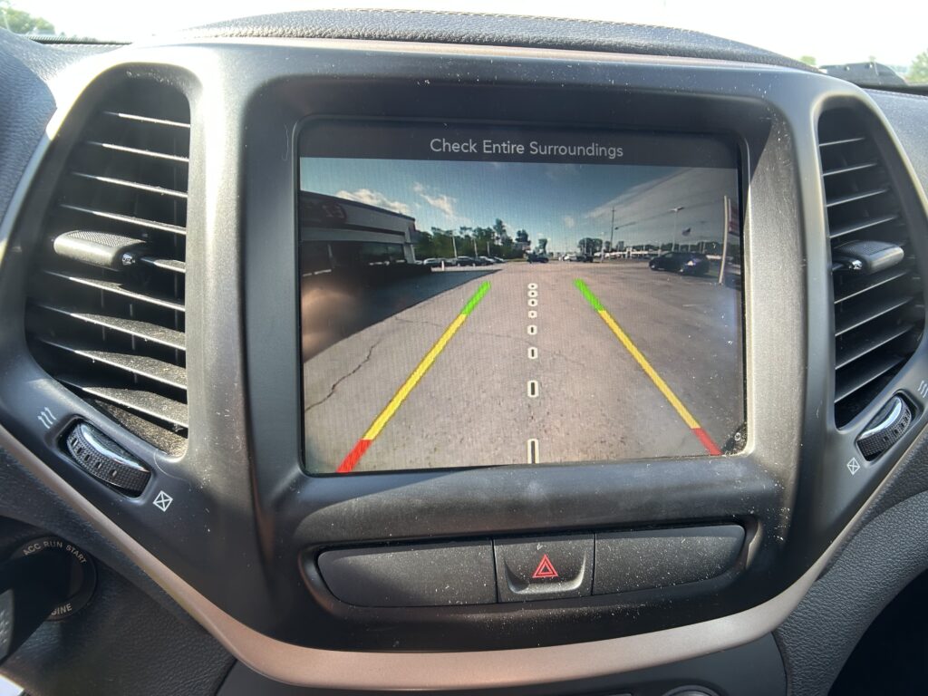 Rearview camera display showing guide lines as the car reverses, with a warning to check surroundings.