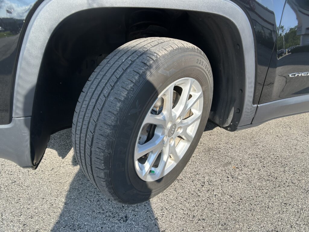 Close-up of a tire and alloy wheel inside the wheel well of a dark SUV, parked on pavement, with the fender visible nearby.