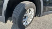 Close-up of a tire and alloy wheel inside the wheel well of a dark SUV, parked on pavement, with the fender visible nearby.