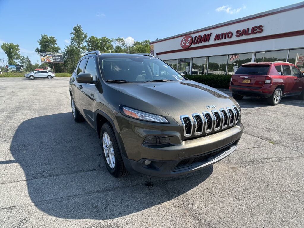 Gray Jeep SUV in the foreground with EZ LOAN AUTO SALES building and red SUV in the background on a sunny day.