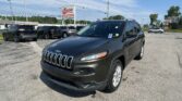 Close-up view of a dark Jeep SUV in a car lot with other vehicles and an EZ LOAN Auto Sales sign in the background under a blue sky.