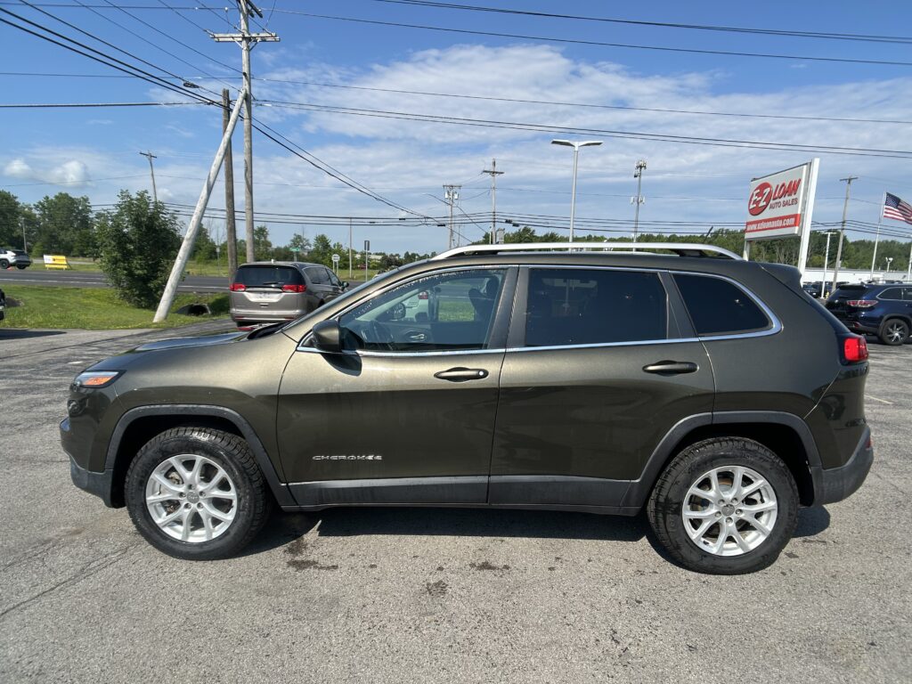 Close-up side view of a gray Jeep Cherokee in a car lot with power lines and a sign for EZ LOAN Auto Sales in the background.