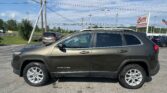 Close-up side view of a gray Jeep Cherokee in a car lot with power lines and a sign for EZ LOAN Auto Sales in the background.