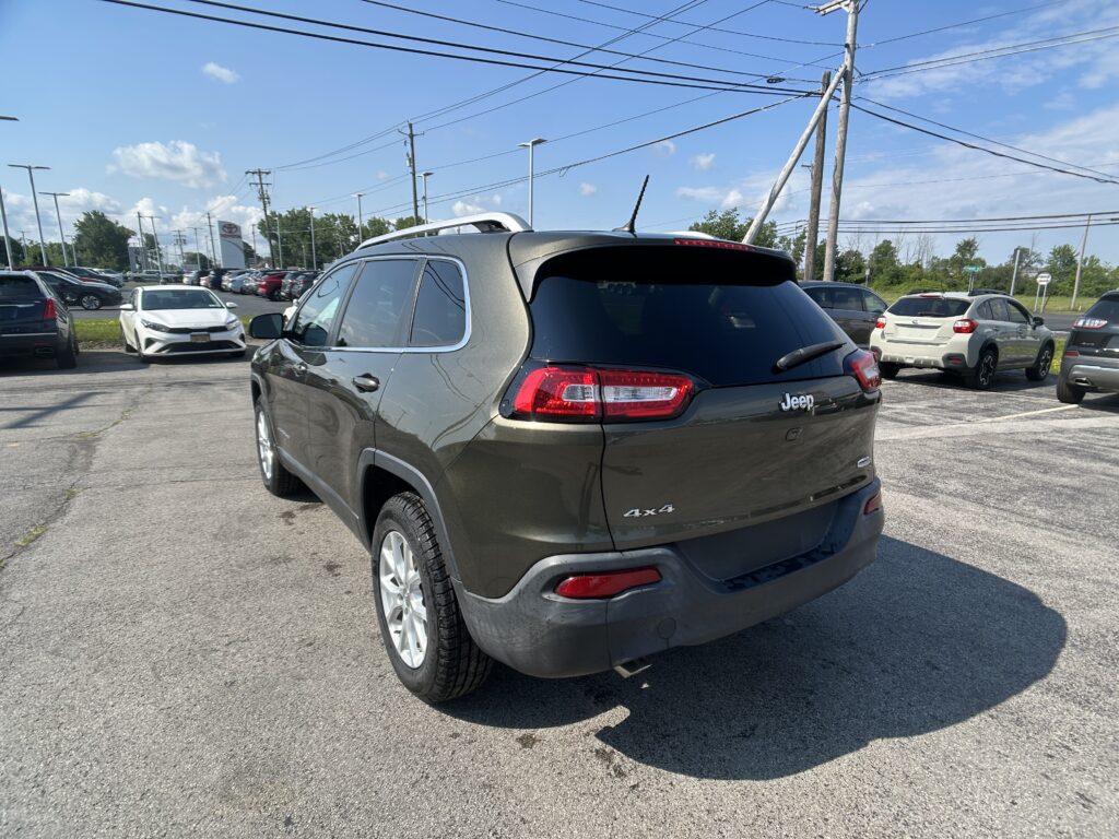 Rear three-quarter view of a gray Jeep Grand Cherokee in a car dealership parking lot