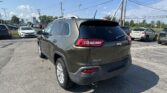 Rear three-quarter view of a gray Jeep Grand Cherokee in a car dealership parking lot