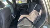 Back seats of a dark fabric SUV interior with seat belts fastened and view of parked cars outside through the windows.