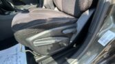 Front interior of a car showing black fabric seats with white stitching, center console, and gear lever in sunlight.