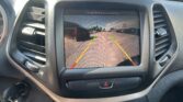 Car dashboard screen showing rearview camera view with parking guidelines as cars line up in a parking lot