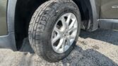 Close-up of a muddy tire and alloy wheel on a dark SUV, with the wheel well and fender visible and water droplets on the body.