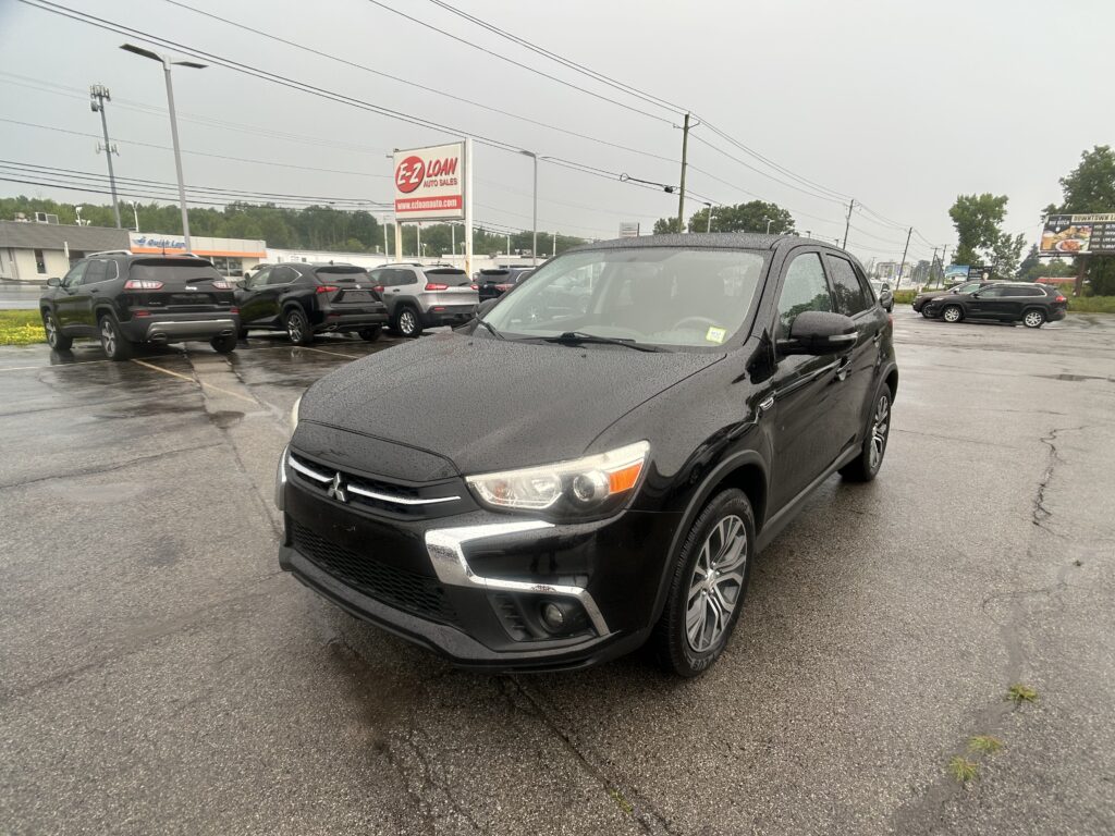 Black SUV in the foreground at a rainy car dealership lot with an EZ Loan Auto Sales sign in the background.