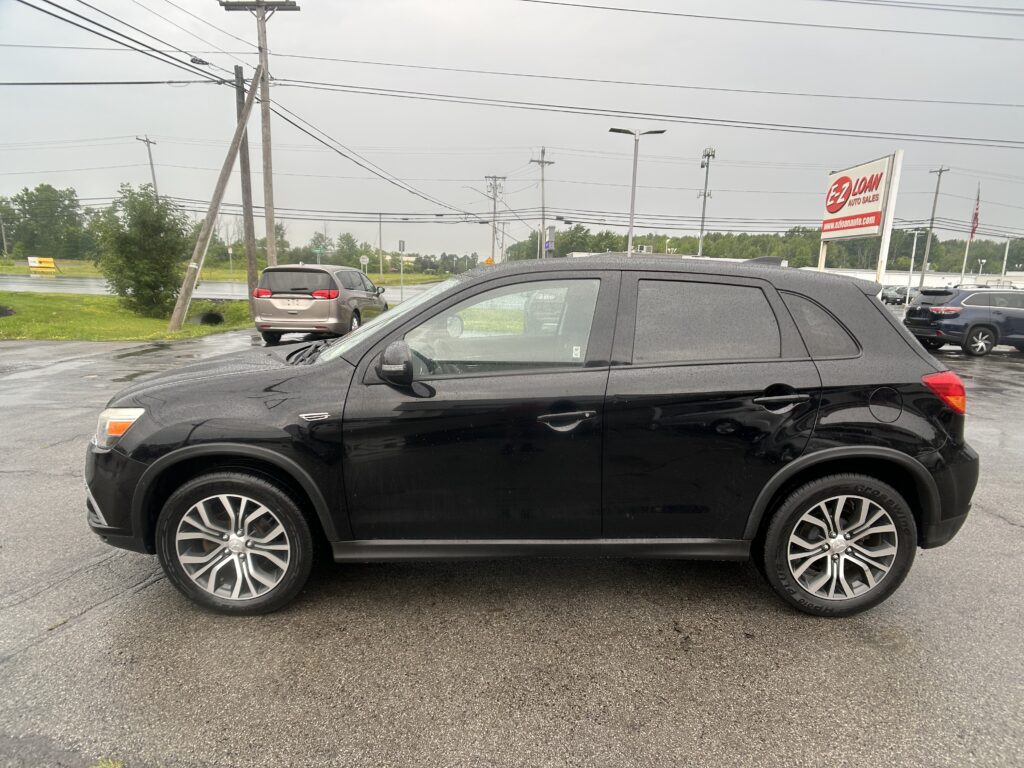 Black SUV in the foreground on a wet parking lot with a red EZ LOAN Auto Sales sign in the distance and utility poles overhead.