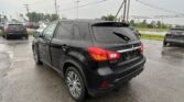 Black Mitsubishi SUV seen from the rear in a wet parking lot, with other cars and power lines in the background.