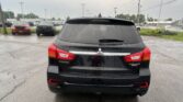 Rear view of a black Mitsubishi Outlander Sport in a rain-soaked parking lot with other vehicles in the background.