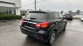 Black Mitsubishi Outlander Sport in a rain-soaked parking lot near a car dealership, with a Toyota sign visible in the background on the building.