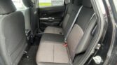 Back seat area of a dark car interior with three seats and headrests, seen from the open rear door on a rainy day outside the window (raindrops visible).