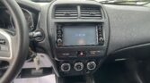 Interior view of a car dashboard from the driver’s seat, showing dual central air vents, a touchscreen display reading 11:00 AM, climate controls, and a gear shifter with papers on the passenger floor mat in front of the center console
