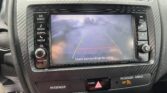 Car infotainment screen showing a rear-view camera with guiding lines; surrounding control buttons labelled Radio, Media, Phone, Seek Track, Home, Tune, and volume knob on a textured dashboard panel.