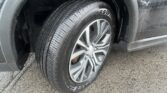 Close-up of a car tire on a silver alloy wheel, with a wet fender and wet pavement nearby, droplets on the body.
