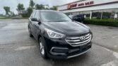 Gray Hyundai SUV in the foreground is parked at a car dealership with an E-Z Loan Auto Sales building behind it on a cloudy day.