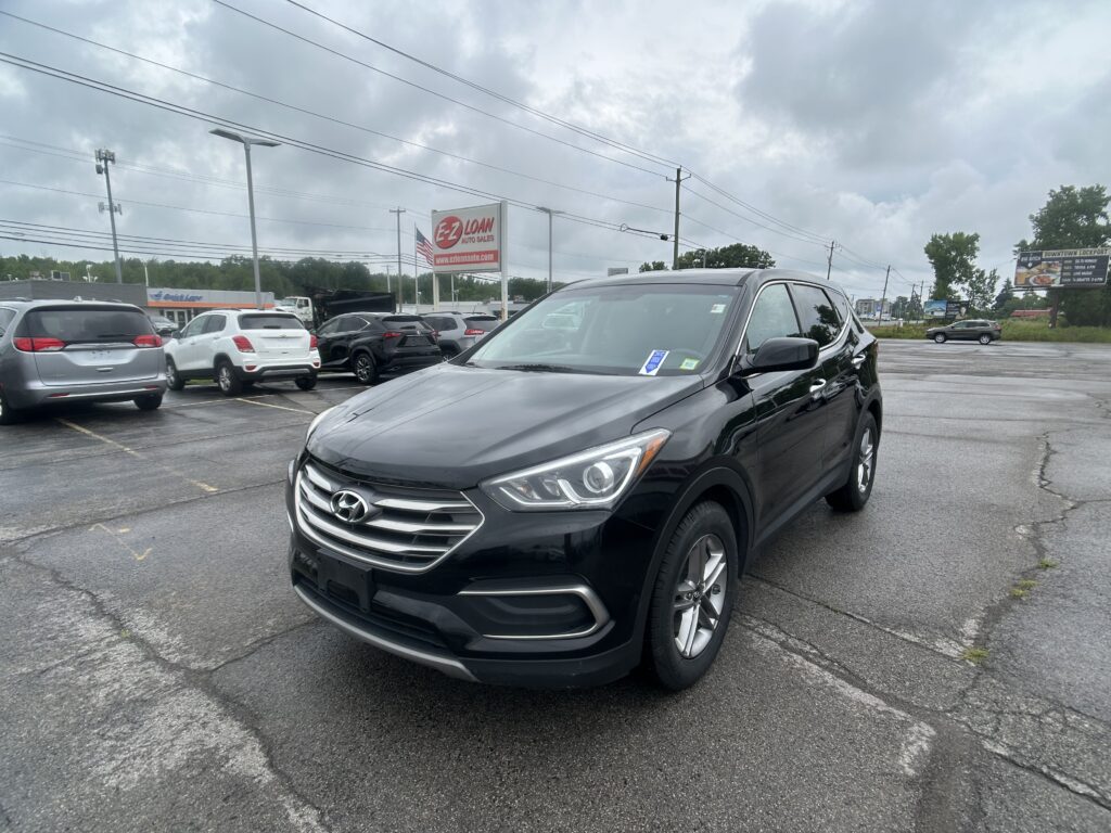 Black Hyundai SUV in foreground of a parking lot with other cars and an EZ LOAN Auto Sales sign in the distance under a cloudy sky