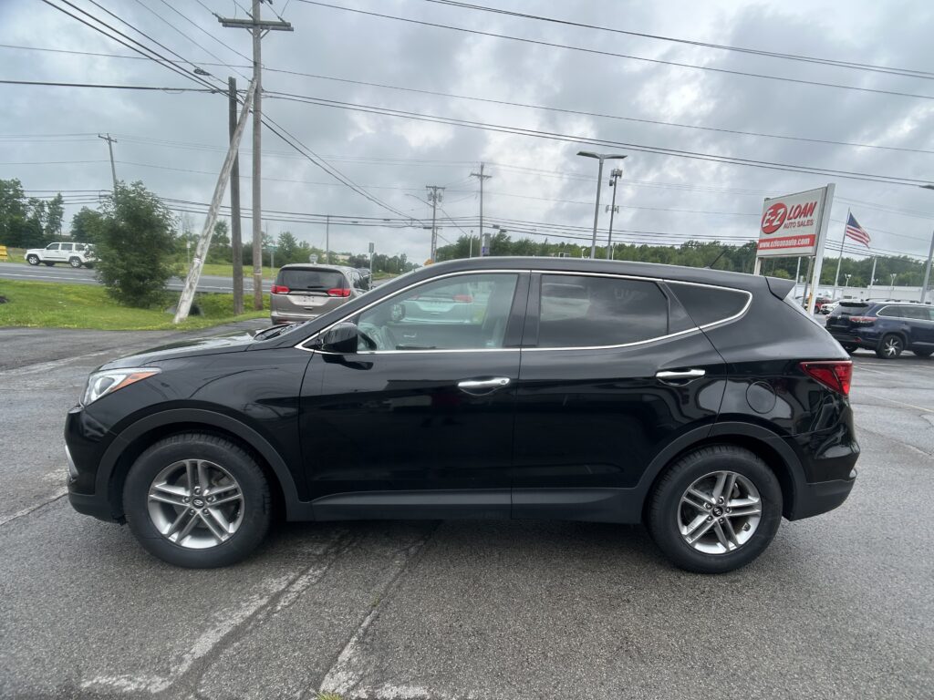 Black SUV in a car dealership lot with EZ Loan Auto Sales sign and an American flag on a cloudy day.
