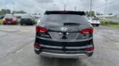 Rear view of a black Hyundai Santa Fe Sport parked in a lot with other vehicles and a cloudy sky above.