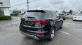 Rear view of a black Hyundai Santa Fe Sport SUV in a parking lot near a Toyota dealership.