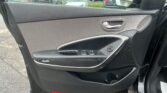 Interior view of a car door panel with a silver door handle, window controls, and speaker; parking lot visible through the window.