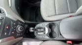 Front interior of a car: gear shifter, climate controls, and grey patterned seats; paper floor mat on the floor.