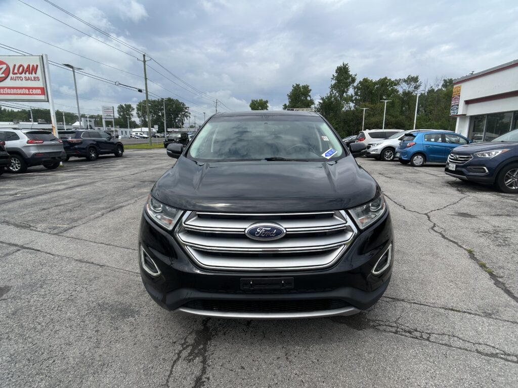Front of a black Ford SUV at a used-car lot, with other vehicles and dealership signs in the background.