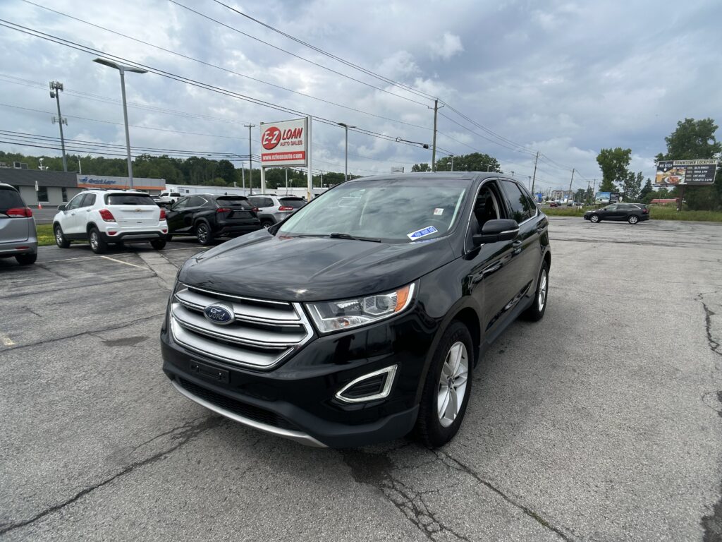 Black Ford SUV in a car dealership lot, foreground, with an EZ LOAN Auto Sales sign and other vehicles around under a cloudy sky.