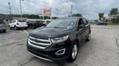Black Ford SUV in a car dealership lot, foreground, with an EZ LOAN Auto Sales sign and other vehicles around under a cloudy sky.
