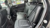 Rear row of a black leather SUV with three seats and visible seat belts, camera angle from the open door outside the car edge.