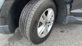 Close-up of a car tire on a silver alloy wheel inside the wheel well of a dark SUV, resting on asphalt
