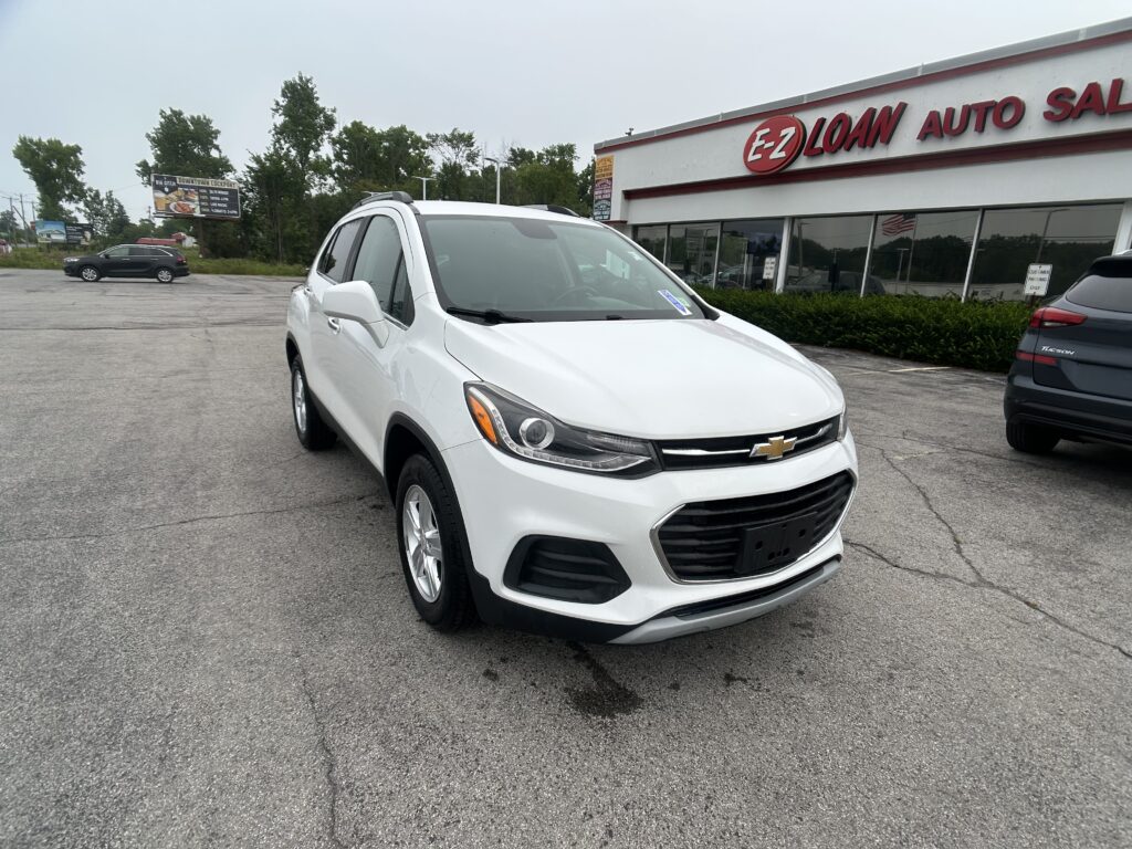White Chevrolet SUV parked diagonally in a dealership lot in front of an EZ Loan Auto Sales building sign.